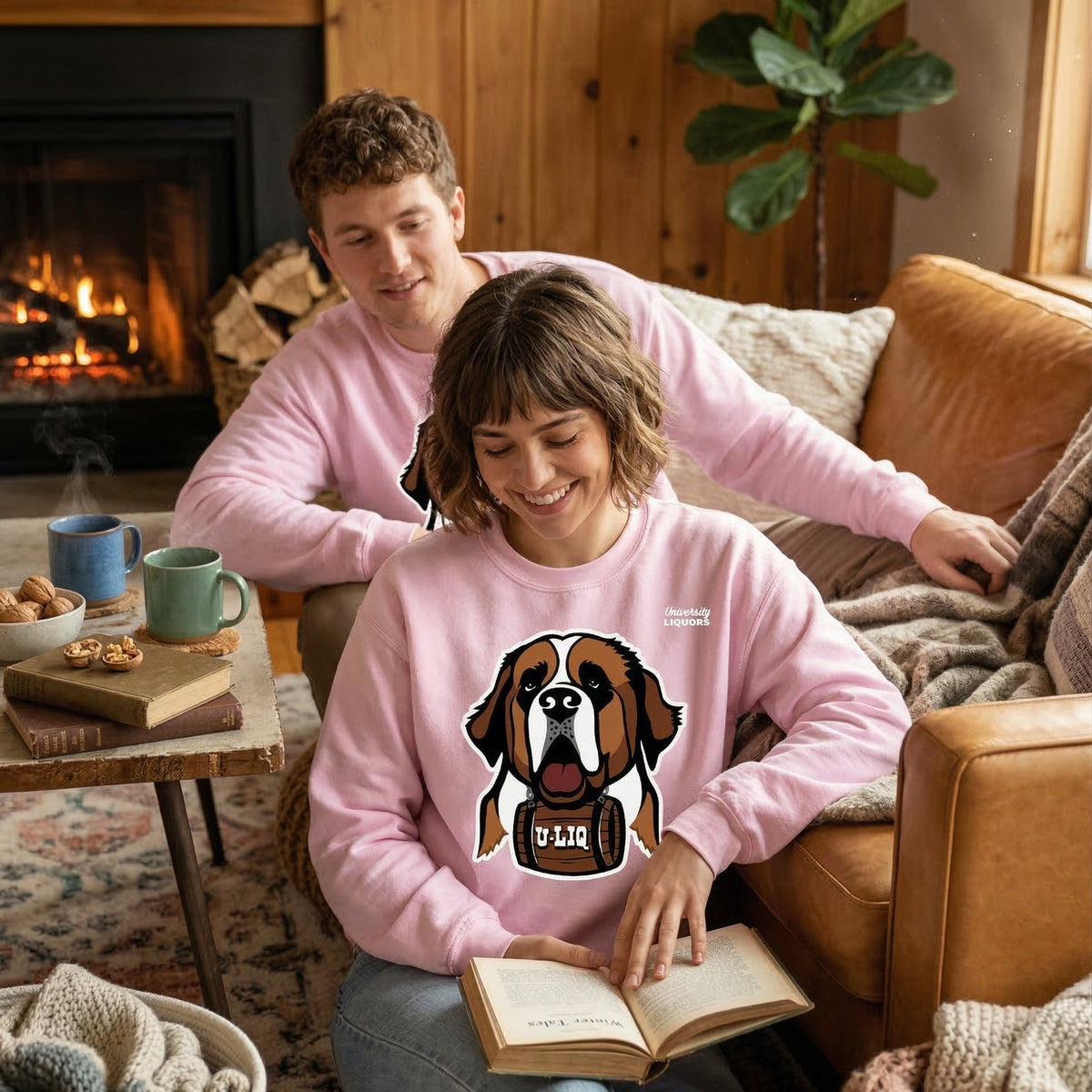 Two people wearing light pink University Liquors sweatshirt in a cozy living room.