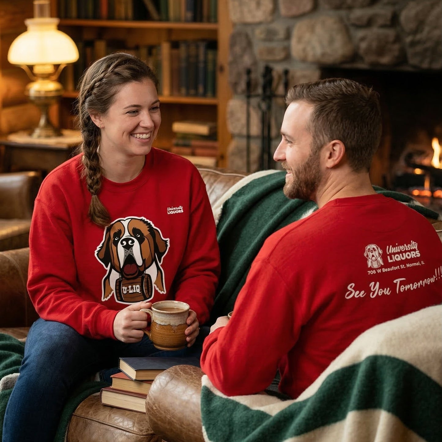 Two people sitting on a couch wearing red University Liquors sweatshirts.