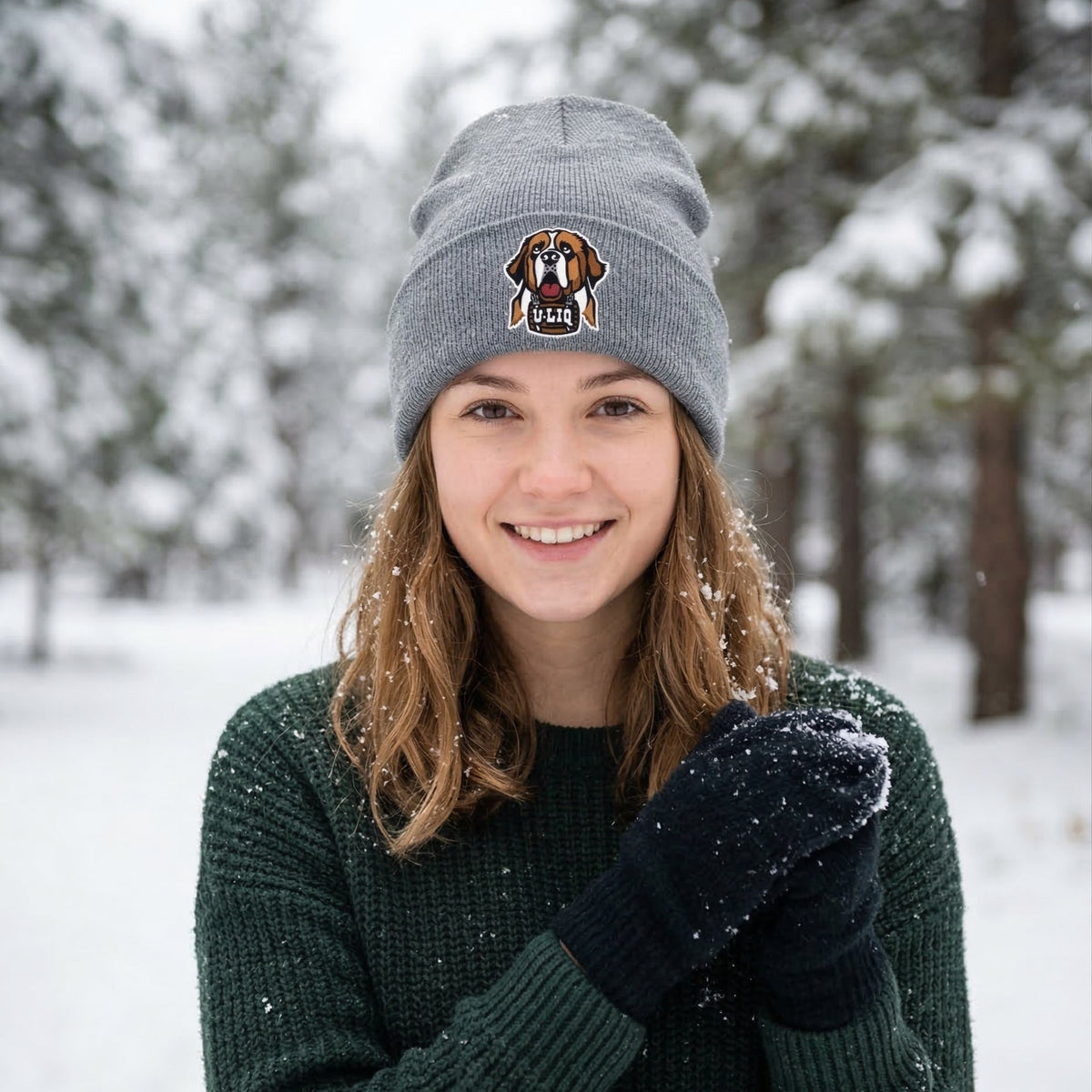 Person wearing a gray beanie with a University Liquors logo in a snowy forest