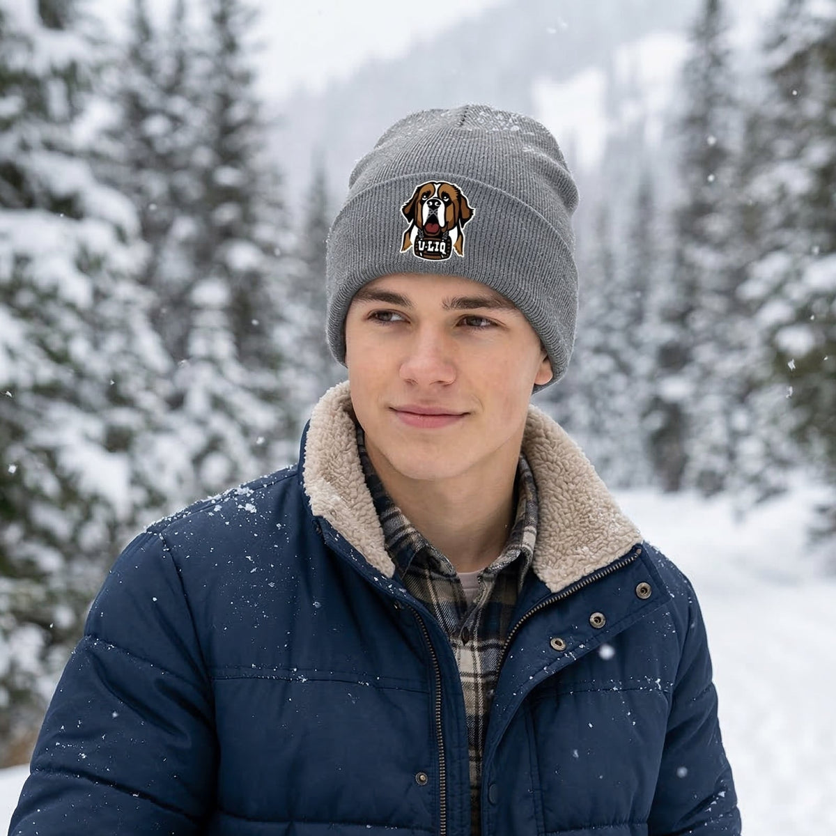 Person wearing a winter coat, beanie with a University Liquors logo, and gloves standing in a snowy forest.
