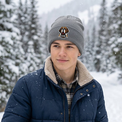Person wearing a winter coat, beanie with a University Liquors logo, and gloves standing in a snowy forest.