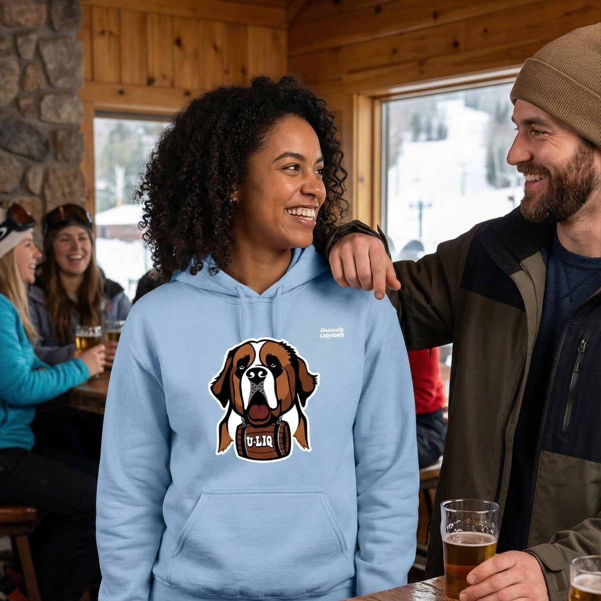 Two people in a pub setting with one wearing a light blue University Liquors hoodie.