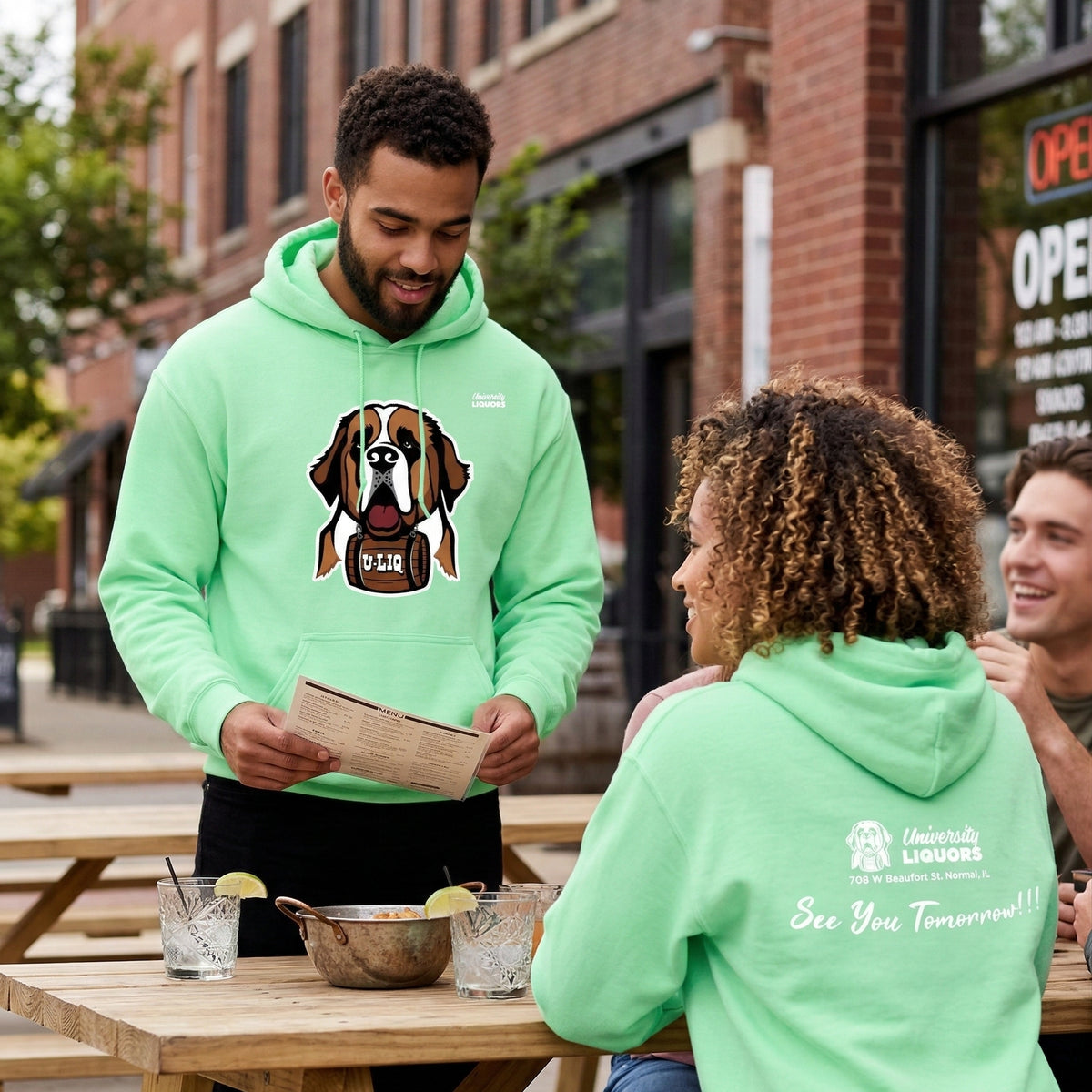 Two people wearing mint green University Liquors hoodie at an outdoor table.